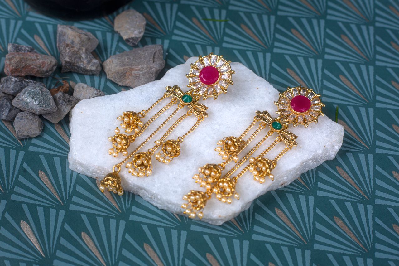 The Art of Drawing Readers In: Your attractive post title goes here Luxurious gold earrings with ruby and emerald stones displayed on white marble, exuding elegance and tradition.
